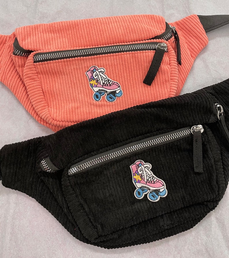 K&ouml;nnte beinhalten: Zwei G&uuml;rteltaschen aus Cord mit Rollschuh-Patches. Die obere G&uuml;rteltasche ist rosa und die untere G&uuml;rteltasche ist schwarz.