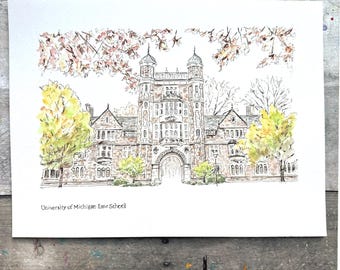 May include: Watercolor illustration of the University of Michigan Law School building. The artwork features the building's facade with an arched entrance, surrounded by trees with yellow and pink foliage. The text "University of Michigan Law School" is printed below the image.
