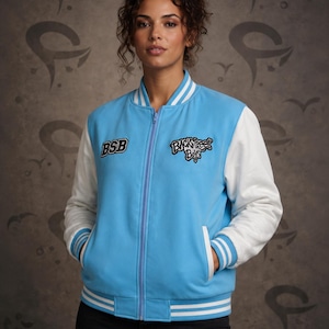 Könnte beinhalten: Eine hellblaue Collegejacke mit weißen Ärmeln und einem Frontreißverschluss. Die Jacke hat weiß gestreifte Rippbündchen an Kragen, Ärmeln und Saum. Auf der Brust befinden sich gestickte Aufnäher mit dem Text BSB und Backstreet Boys in Schwarz.