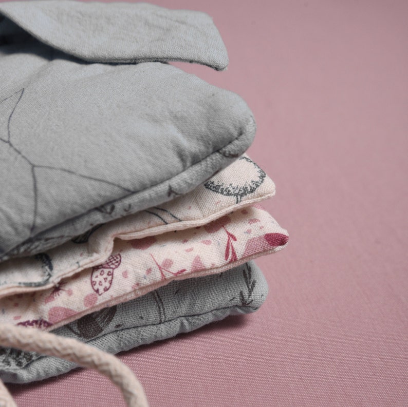 May include: A stack of four fabric squares with different floral patterns. The top square is a light blue color with a simple design, the second square is a cream color with a floral pattern, the third square is a light pink color with a floral pattern, and the bottom square is a light blue color with a simple design.