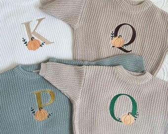 May include: Four knitted sweaters with embroidered letters and pumpkins. The sweaters are in white, beige, light blue, and dark green.