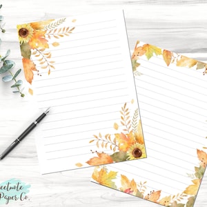 May include: Two sheets of lined stationery paper with a fall theme. The paper has a border of watercolor sunflowers, leaves, and branches in shades of yellow, orange, and brown. The text "Sweetnote Paper Co." is in the bottom left corner.