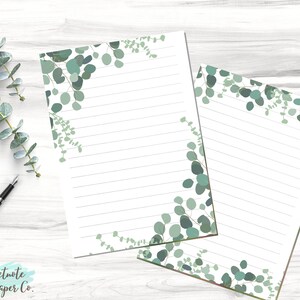 Könnte beinhalten: Zwei Blätter liniertes Briefpapier mit einem Eukalyptus-Blatt-Rand. Das Papier ist weiß mit hellgrauen Linien. Die Blätter sind grün und grau.