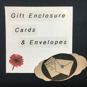 May include: A white card with the text "Gift Enclosure Cards & Envelopes" printed on it. A red flower is in the bottom left corner. A brown envelope with a blue heart is in the bottom right corner. The envelope has the text "Roma's Card Kits by YOU" printed on it.