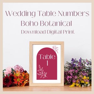 May include: A printable wedding table number card with a burgundy arch and botanical leaves. The text "Table 1" is in a white sans-serif font.