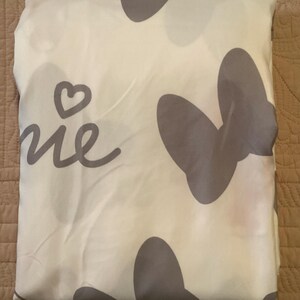 May include: A white fabric with a grey butterfly design and the word "Home" written in cursive. The fabric has a heart shape in the top left corner.