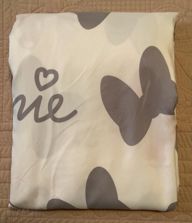 May include: A white fabric with a grey butterfly design and the word "Home" written in cursive. The fabric has a heart shape in the top left corner.