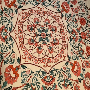 May include: Cream-colored textile with a repeating floral pattern in coral, teal, and brown. The design features large stylized flowers, leaves, and intricate circular motifs, creating a symmetrical and ornate composition.