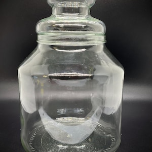 May include: A clear glass jar with a rounded lid and a wide, cylindrical body. The jar has a slightly flared base and a narrow neck. The glass is transparent, allowing a view of the contents. The jar is suitable for storage.
