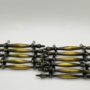 May include: A collection of antique brass-colored cabinet handles. Each handle has a curved, cylindrical grip with decorative finials at each end. The handles are arranged in rows, showcasing their design and finish. Hardware for furniture restoration.