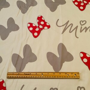 May include: White fabric with a repeating pattern of grey bows and red bows with white polka dots. The text "Minnie" is printed in grey on the fabric.