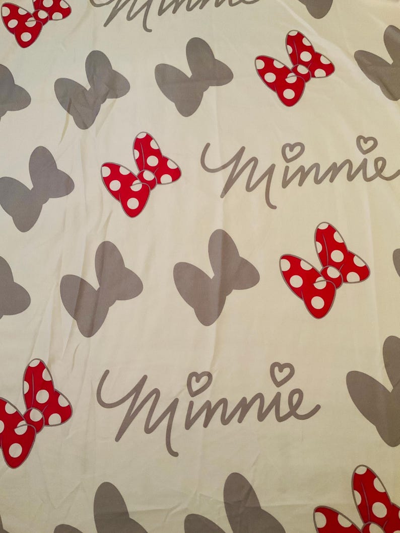 May include: White fabric with a repeating pattern of grey bows and red bows with white polka dots. The text "Minnie" is written in grey cursive.