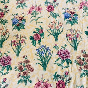 May include: A floral pattern featuring various flower bouquets in shades of pink, purple, blue, and yellow. The flowers are arranged on a light yellow background with a subtle textured pattern. The design includes roses, lilies, and other floral arrangements.