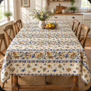 May include: A rectangular tablecloth featuring a cream-colored base with repeating horizontal bands of blue floral patterns and illustrations of roosters in shades of yellow, brown, and red. The fabric drapes over a wooden table surrounded by chairs.