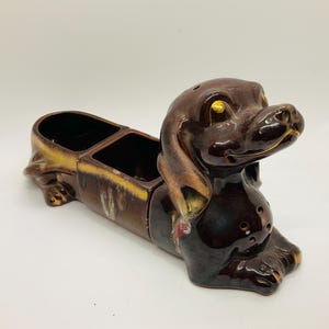May include: A brown ceramic dachshund figurine with gold accents. The dachshund has two divided compartments on its back, perfect for holding small items.