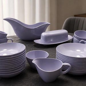 May include: A large set of lavender-colored ceramic dinnerware including stacked bowls, a gravy boat, a butter dish with a lid, and several handled cups. The collection features a smooth, glossy finish and uniform light purple coloring throughout.