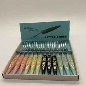 May include: A set of vintage little forks in a box. The forks have colorful handles in pink, yellow, black, and blue, with a floral design. The box has the words "SPECIAL QUALITY" and "LITTLE FORKS" printed on it.