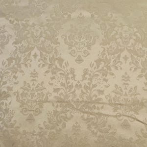 May include: A beige fabric with a repeating damask pattern. The design features stylized floral and scroll motifs in a lighter shade of beige, creating a subtle contrast. The fabric has a slightly textured appearance, suggesting a woven material.