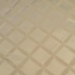 May include: Cream-colored fabric with a quilted diamond pattern. Each diamond features a leaf-like design, creating a textured surface. The fabric has a subtle sheen, suggesting a satin or similar material.