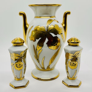 May include: A white porcelain vase with gold accents and a matching pair of salt and pepper shakers. The vase features a gold floral design, with gold handles. The salt and pepper shakers have a similar design. The set is a decorative kitchenware item.