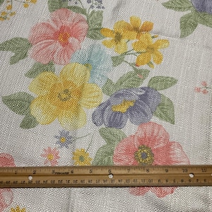 May include: Floral fabric with a light gray background, featuring large, colorful flowers in shades of pink, yellow, blue, and purple. A wooden ruler, marked in inches, rests on the fabric.