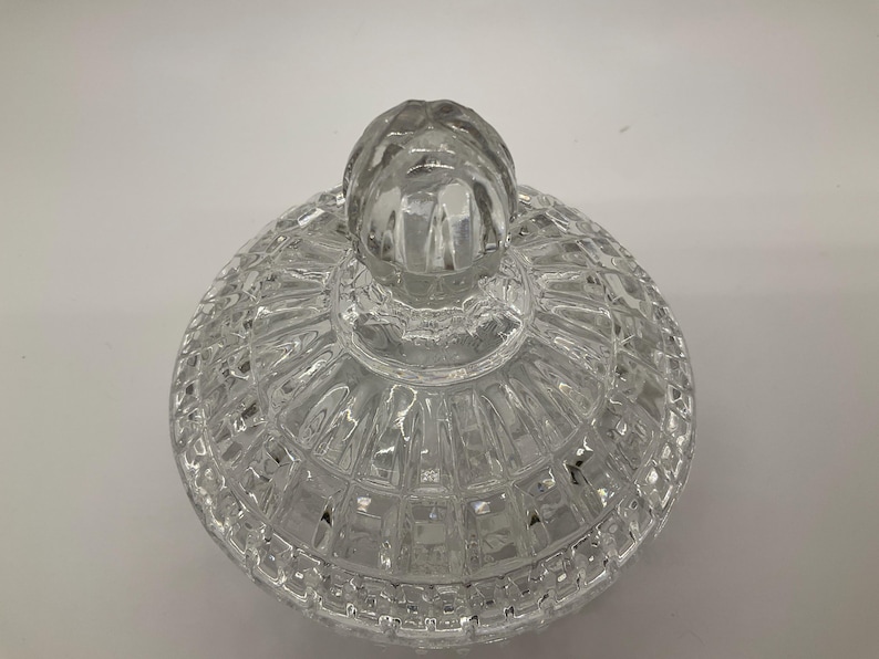 May include: A clear, glass candy dish lid with a textured, geometric pattern. The lid has a rounded shape with a knob on top for easy handling. The dish is designed to sit on a matching base, creating a decorative storage container.