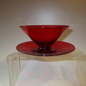 May include: A red glass bowl with a matching saucer. The bowl has a wide, flared rim and a pedestal base.