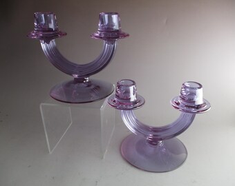 Puede incluir: Dos candelabros de vidrio lavanda con un diseño curvo único. Cada candelabro tiene dos portavelas y una base ancha.