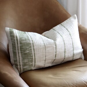 May include: A brown leather armchair with a white and green striped pillow. The chair has a matching ottoman and is sitting on a patterned rug.