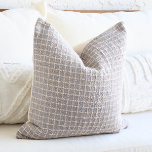 May include: A gray and beige patterned throw pillow with a textured weave. The pillow is sitting on a white couch.