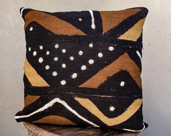 May include: A brown, black, and white patterned throw pillow with a geometric design. The pillow is made of a woven fabric and has a fringed edge.