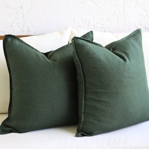 May include: Two dark green linen throw pillows on a white couch.