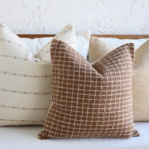 May include: Four decorative throw pillows in a neutral color palette. The pillows are arranged on a white couch. The pillows are made of different fabrics and have different patterns. The pillows are a great way to add a touch of style and comfort to any room.