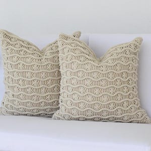 May include: Two cream-colored throw pillows with a woven, textured pattern. The pillows are on a white couch.