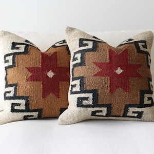 May include: Two decorative throw pillows with a geometric pattern in shades of brown, black, white, and red. The pillows feature a star design with a geometric border.