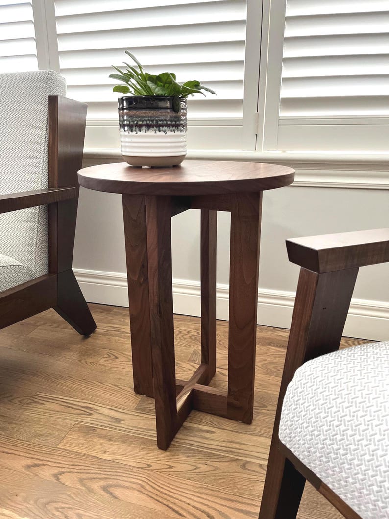 Op de afbeelding: Een donkerbruine houten bijzettafel met een rond blad en een eenvoudig, modern ontwerp. De tafel heeft &eacute;&eacute;n plank en wordt ondersteund door vier poten.