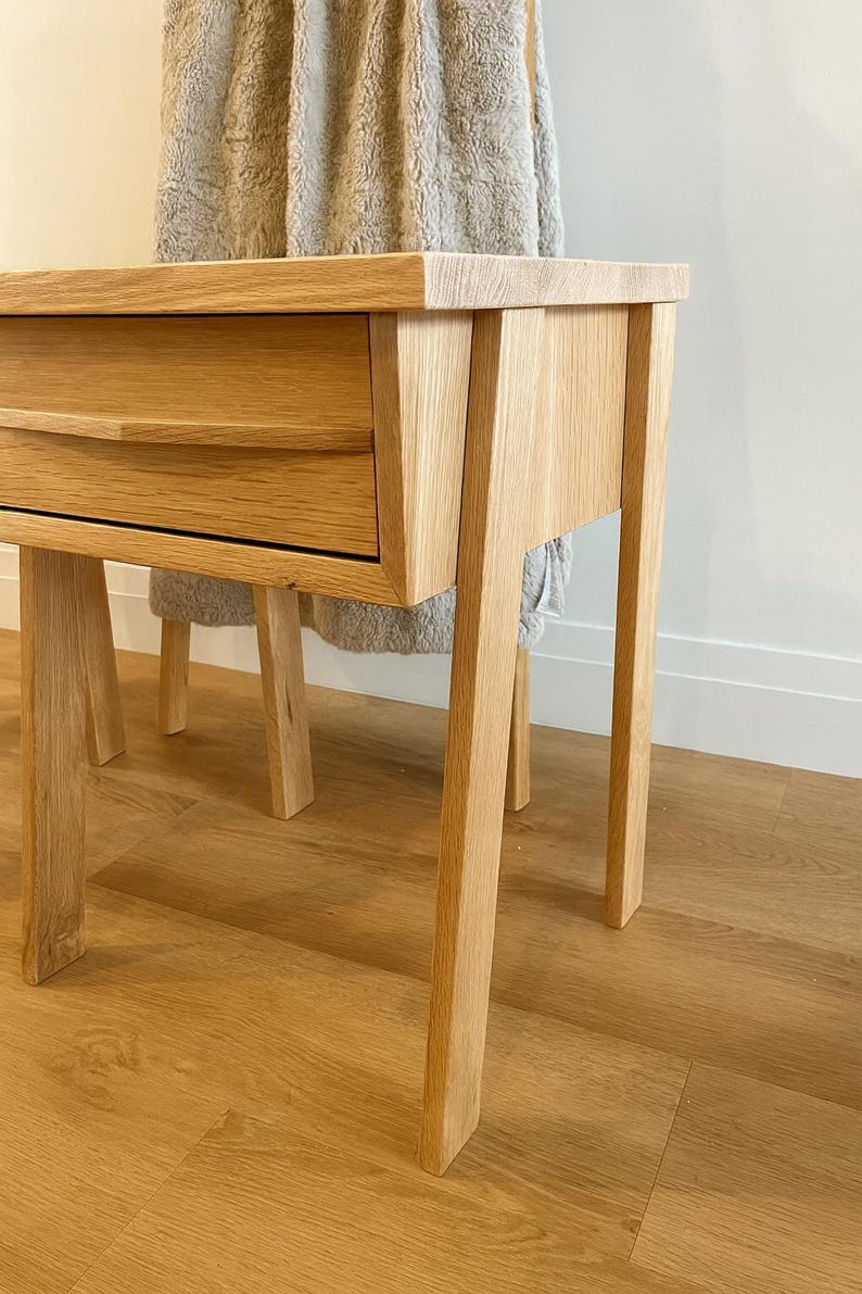 Pu&ograve; includere: Un tavolino in legno di rovere chiaro con un cassetto. Il tavolo ha un piano rettangolare e quattro gambe dritte. Il cassetto ha una maniglia curva. Il tavolo &egrave; appoggiato su un pavimento in legno marrone chiaro.