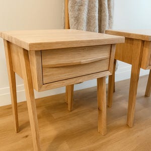 Pu&ograve; includere: Due comodini in legno di rovere chiaro con un cassetto e quattro gambe angolate. I comodini hanno un design semplice e moderno e sono realizzati in legno chiaro. Il cassetto ha una maniglia curva. I comodini sono posizionati su un pavimento in legno chiaro.