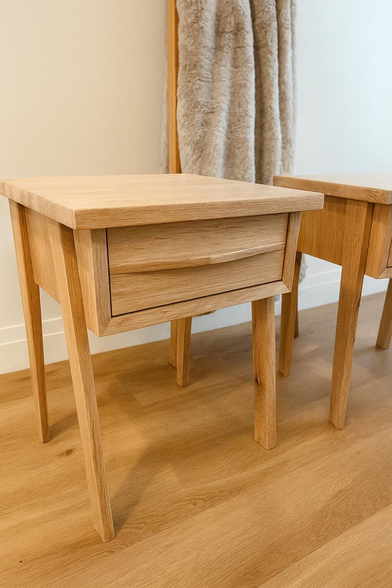 Pu&ograve; includere: Due comodini in legno di rovere chiaro con un cassetto e quattro gambe angolate. I comodini hanno un design semplice e moderno e sono realizzati in legno chiaro. Il cassetto ha una maniglia curva. I comodini sono posizionati su un pavimento in legno chiaro.