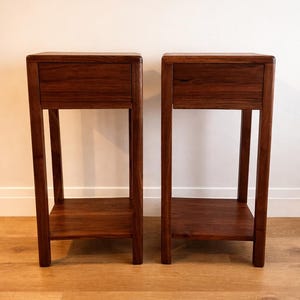 Puede incluir: Dos mesas auxiliares de madera a juego. Cada mesa tiene un caj&oacute;n, un estante inferior y cuatro patas. Las mesas son de madera marr&oacute;n oscuro y est&aacute;n colocadas contra una pared blanca y un suelo de madera marr&oacute;n claro.