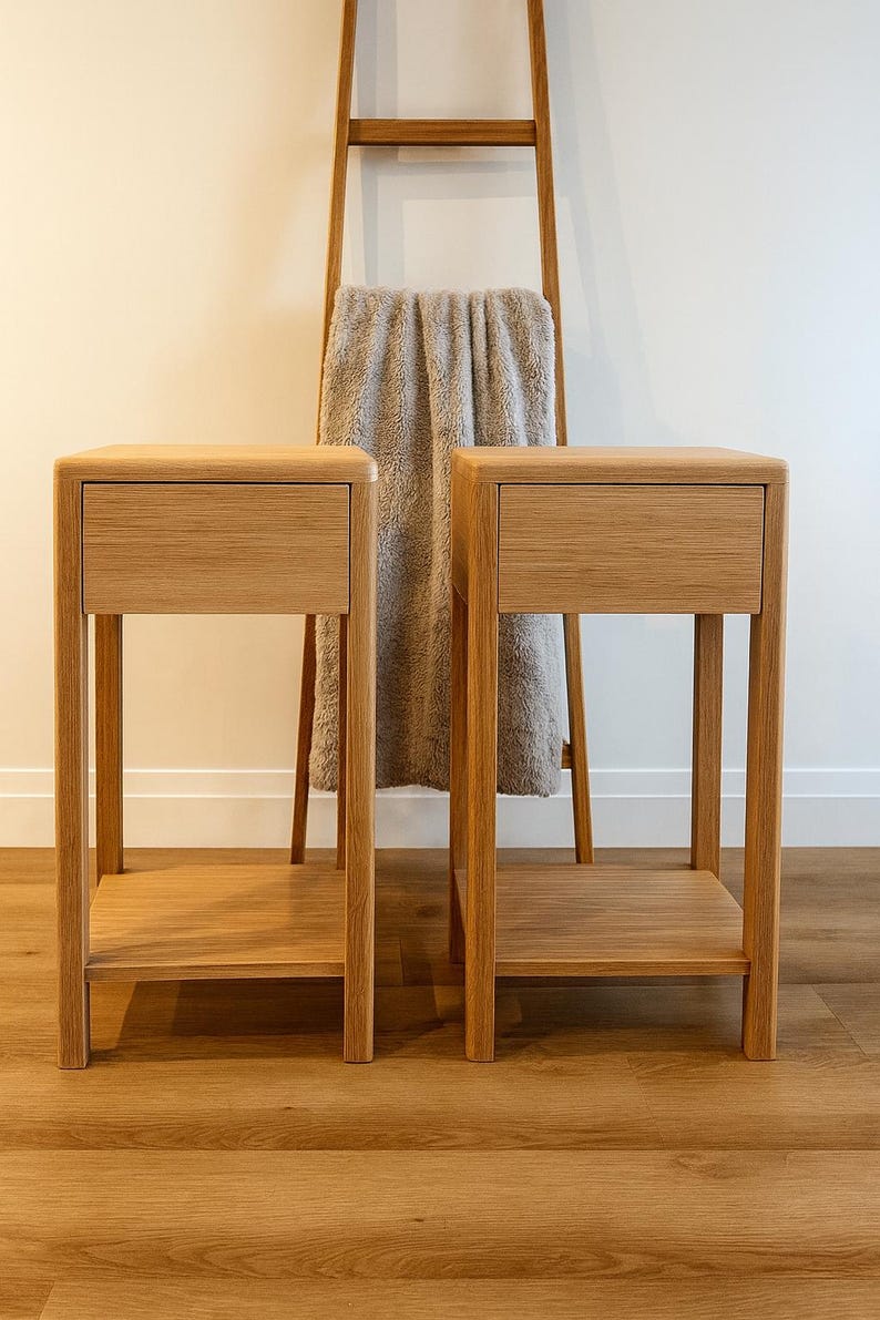 Puede incluir: Dos mesitas de noche de madera a juego con cajones y estantes inferiores. Las mesas son de madera de color claro y tienen un dise&ntilde;o sencillo y moderno. Una escalera de madera con una manta gris est&aacute; en el fondo.