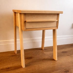 Pu&ograve; includere: Un comodino in legno chiaro con due cassetti e quattro gambe angolate. Il comodino &egrave; realizzato in legno chiaro e ha un design semplice e moderno. I cassetti hanno un piccolo bordo per una facile apertura. Il comodino &egrave; alto 61 cm.