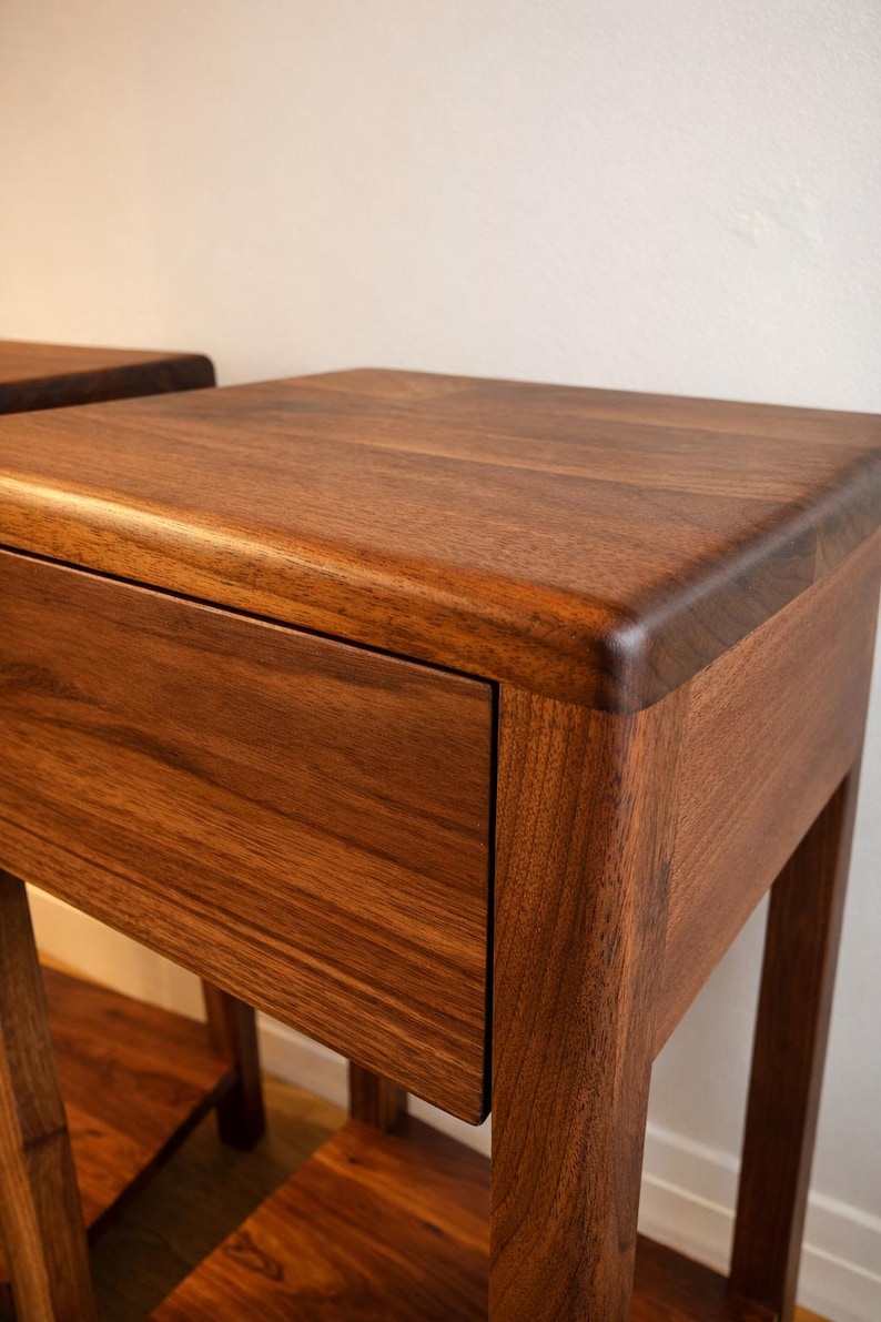 Puede incluir: Dos mesitas de noche de madera con un acabado marr&oacute;n c&aacute;lido. Cada mesa tiene un caj&oacute;n y un estante inferior. La veta de la madera es visible, dando un aspecto natural. El dise&ntilde;o es minimalista y moderno, adecuado para un dormitorio.
