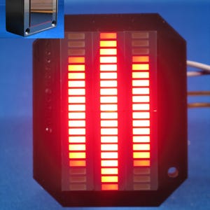 Peut inclure: Composant électronique noir avec trois colonnes de lumières LED rouges et oranges. Les lumières sont allumées, créant un affichage visuel. Une petite boîte noire est dans le coin supérieur gauche. Le fond est bleu uni.