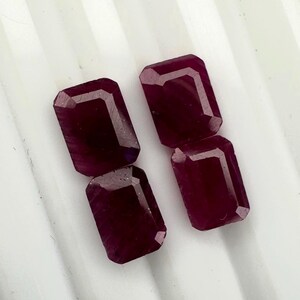 Puede incluir: Tres piedras preciosas sueltas de corte rectangular con un color rojo oscuro profundo y saturado. Cada piedra presenta bordes facetados que reflejan la luz, mostrando una superficie pulida y un tono carmesí rico y uniforme en todas.