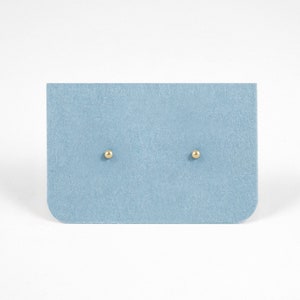 May include: A pair of gold stud earrings displayed on a light blue velvet background.