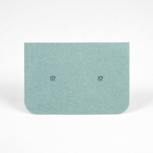 May include: A pair of small, blue gemstone stud earrings on a light blue felt background.