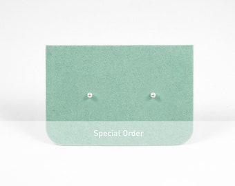 Op de afbeelding: Een paar zilveren oorbelletjes op een groene kaart met de tekst "Special Order".
