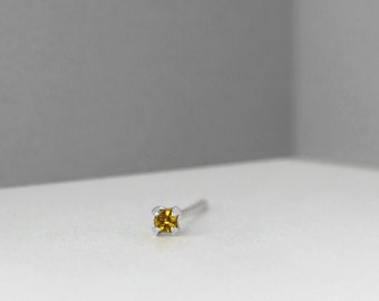 Può includere: Un piccolo anello per il naso in argento con una singola pietra preziosa gialla trasparente.