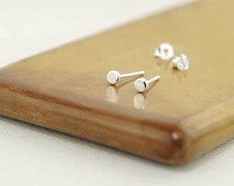 May include: A pair of silver stud earrings with round, flat tops. The earrings are on a wooden surface.